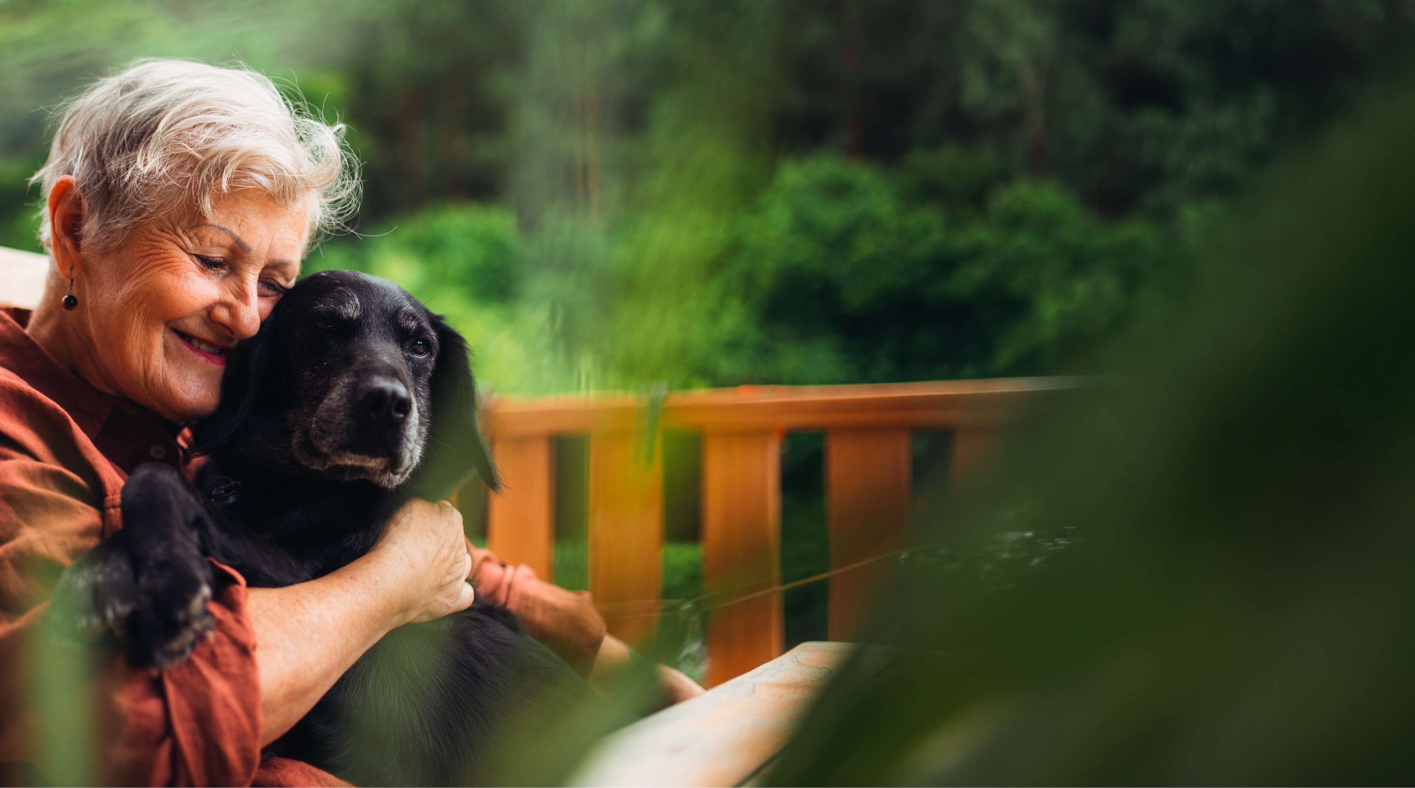 An older woman embracing a black Labrador in a garden